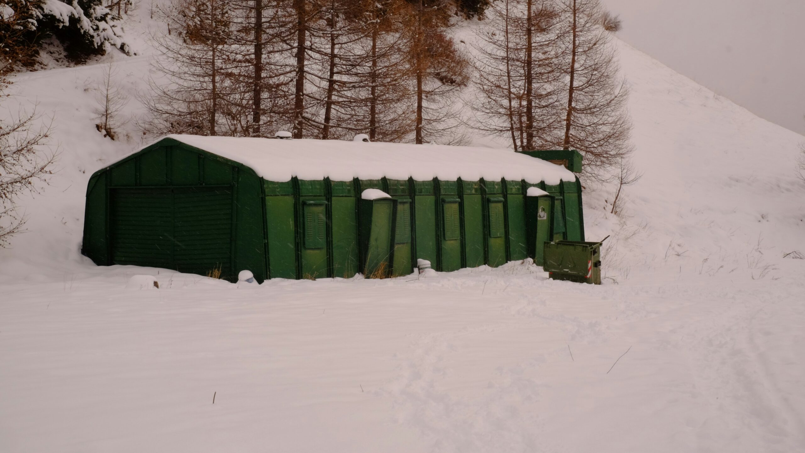a green shed sitting on top of a snow covered slope